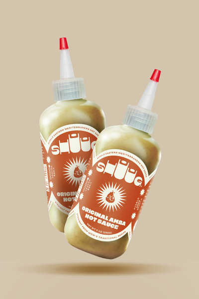 Two bottles of Shuug hot sauce on a beige background